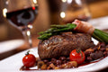 Steak with asparagus and tomatoes on a plate with a glass of red wine in the background.